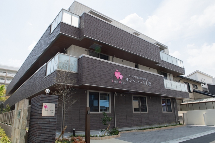 黒いタイル張りの3階建て介護施設の建物外観。玄関前には看板があり、モダンな設計。